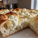 A close-up cross-section view of a freshly baked white pizza showing the airy crust and dollops of creamy ricotta cheese topping.