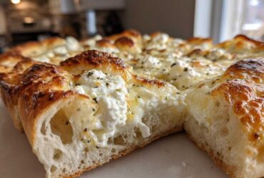 A close-up cross-section view of a freshly baked white pizza showing the airy crust and dollops of creamy ricotta cheese topping.