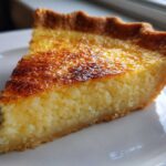 A close-up slice of homemade buttermilk pie showing a creamy, textured filling and a deeply browned top crust.