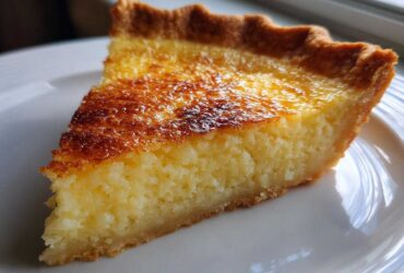 A close-up slice of homemade buttermilk pie showing a creamy, textured filling and a deeply browned top crust.