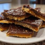 A stack of rich graham cracker toffee squares featuring a thick caramel layer and dark chocolate topping sprinkled with sea salt.