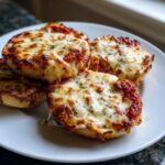 Close-up of four golden brown pizza bagels topped with melted, bubbly mozzarella cheese and herbs.