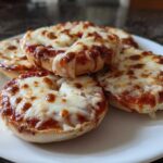 A plate of freshly made pizza bagels topped with melted, bubbly mozzarella cheese and tomato sauce.