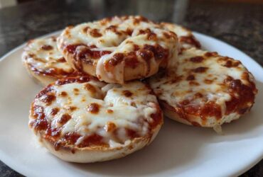 A plate of freshly made pizza bagels topped with melted, bubbly mozzarella cheese and tomato sauce.