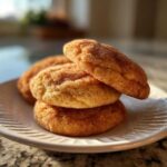 Three soft, thick snickerdoodle cookies stacked on a white plate, coated in cinnamon sugar.