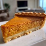 A close-up, sunlit slice of rich, orange sweet potato pie with a flaky crust.