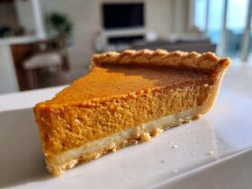 A close-up, sunlit slice of rich, orange sweet potato pie with a flaky crust.