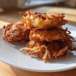 A stack of crispy, golden brown Amish Onion Fritters resting on a white plate.