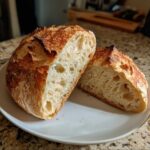 A loaf of artisan bread, cut in half, showing an open, airy crumb structure.
