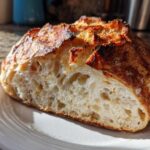 A freshly baked loaf of artisan bread, cut in half to show the airy, open crumb structure and dark, crusty exterior of the bread.