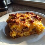 A square serving of bacon cheeseburger casserole topped with bubbly, melted cheddar cheese and browned ground meat.