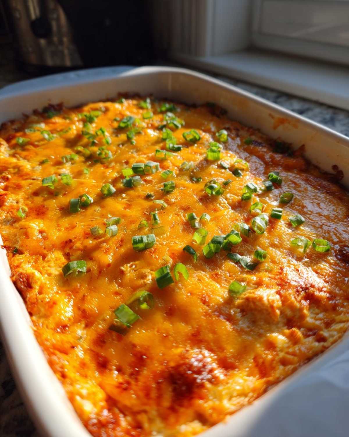 Close-up of a hot, bubbly buffalo chicken dip topped with melted cheddar and sliced green onions in a white baking dish.