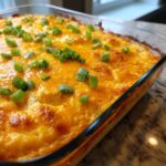 Close-up of a baked buffalo chicken dip topped with melted cheddar cheese and chopped green onions.