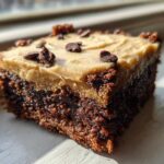 A single square of rich, dark banana bread brownies topped with light brown frosting and chocolate chips.