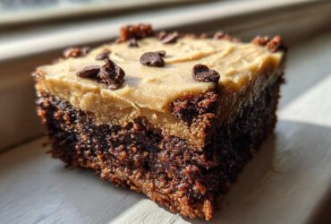 A single square of rich, dark banana bread brownies topped with light brown frosting and chocolate chips.