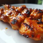 Close-up of perfectly grilled bang bang chicken skewers coated in a glossy, spicy orange sauce.