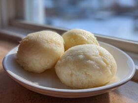 Three perfectly shaped scoops of pale yellow fufu served on a small white dish near a window.