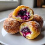 Close-up of several sugared Blueberry Pie Bombs stacked, one cut open showing creamy filling and rich blueberry jam.