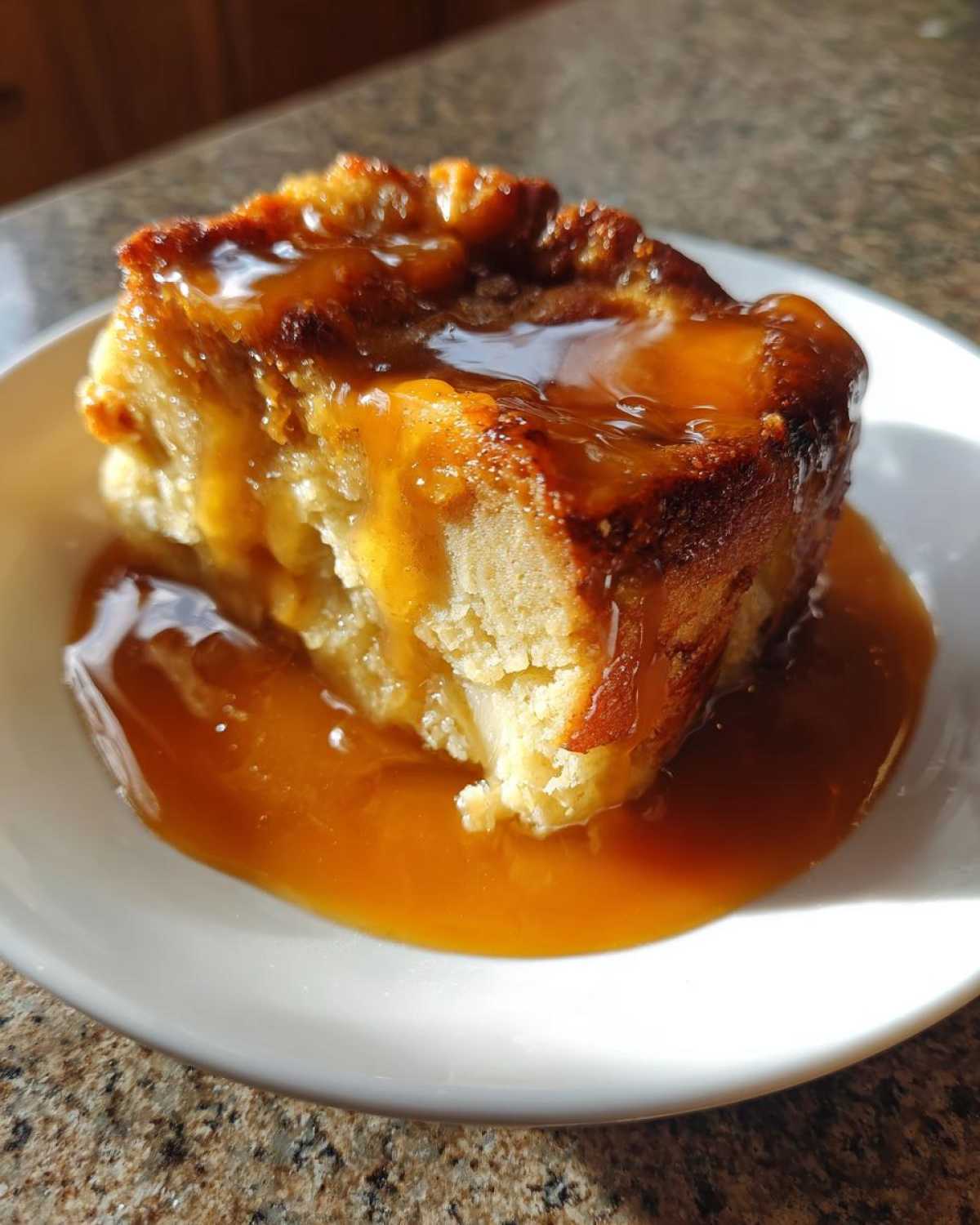 A close-up of a single serving of bread pudding with bourbon sauce generously poured over the top.
