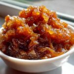 Close-up of rich, dark brown caramelized onions piled high in a small white serving bowl.