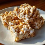 Three squares of gooey, white-coated avalanche cookies stacked on a white plate, catching the sunlight.