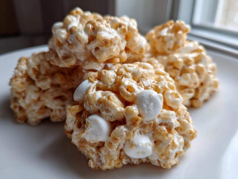 Close-up of three golden-brown avalanche cookies made with cereal and marshmallows, sitting on a white plate.