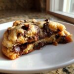 A close-up of a broken chewy chocolate chip cookies revealing a gooey, molten chocolate center on a white plate.