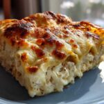 A close-up of a rich, cheesy slice of chicken alfredo lasagna with a golden-brown, bubbly top.