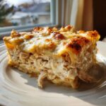 A generous slice of creamy chicken alfredo lasagna showing shredded chicken filling and a bubbly, browned cheese topping.