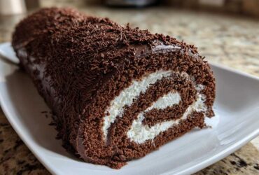 Cross-section of a rich chocolate yule log cake showing a swirl of white cream filling.
