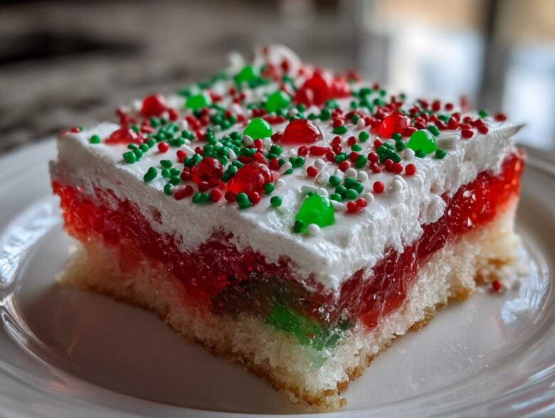 Close-up of a slice of Christmas poke cake featuring layers of white cake, red and green gelatin, whipped topping, and holiday sprinkles.