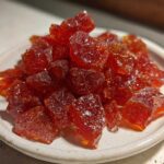 Close-up of a small white dish filled with sparkling, deep red chunks of homemade cinnamon rock candy.