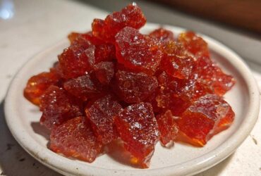 Close-up of a small white dish filled with sparkling, deep red chunks of homemade cinnamon rock candy.