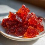 Close-up of shattered, deep red, translucent pieces of cinnamon rock candy piled on a small plate.