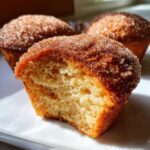 A close-up view of a french toast muffin broken in half, showing the soft interior and a thick cinnamon sugar topping.