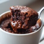 A spoonful of rich, gooey Cottage Cheese Microwave Brownie being lifted from a white mug.