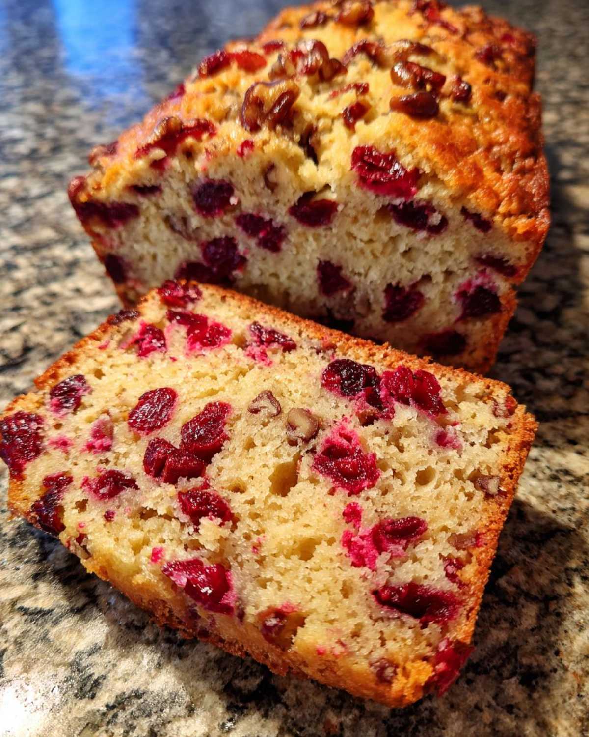A close-up of a moist slice of cranberry walnut bread, showing bright red cranberries and nuts embedded in the crumb.