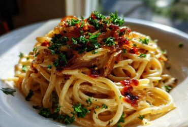 Close-up of creamy caramelized onion pasta tossed in sauce and topped with crispy onions and fresh parsley.