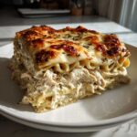 A generous slice of creamy chicken lasagna showing layers of pasta, shredded chicken filling, and a browned, cheesy top.