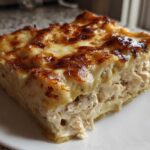 A thick, square slice of creamy chicken lasagna showing shredded chicken filling and a bubbly, browned cheese top.