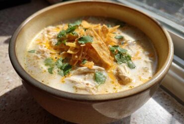 Close-up of a bowl of creamy chicken tortilla soup topped with tortilla strips, shredded cheese, and cilantro.