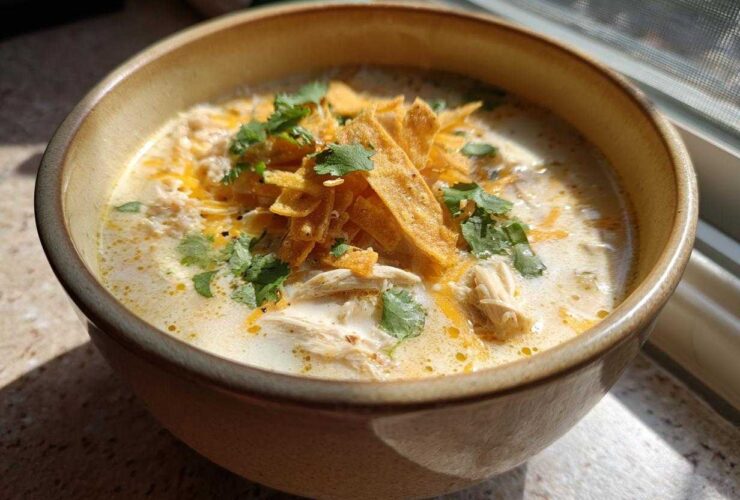 Close-up of a bowl of creamy chicken tortilla soup topped with tortilla strips, shredded cheese, and cilantro.