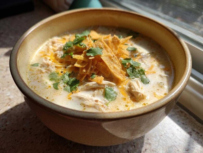 Close-up of a bowl of creamy chicken tortilla soup topped with tortilla strips, shredded cheese, and cilantro.