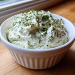 A close-up of creamy dill dip generously topped with fresh chopped dill, served in a white fluted ramekin.