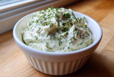 A close-up of creamy dill dip generously topped with fresh chopped dill, served in a white fluted ramekin.