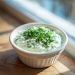 Close-up of creamy dill dip in a white ramekin, generously topped with fresh, bright green dill.