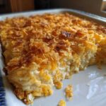 A close-up of a creamy funeral potatoes recipe casserole baked in a dish with a golden, crunchy cornflake topping.