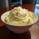 A close-up of incredibly creamy, fluffy mashed potatoes piled high in a white serving bowl.