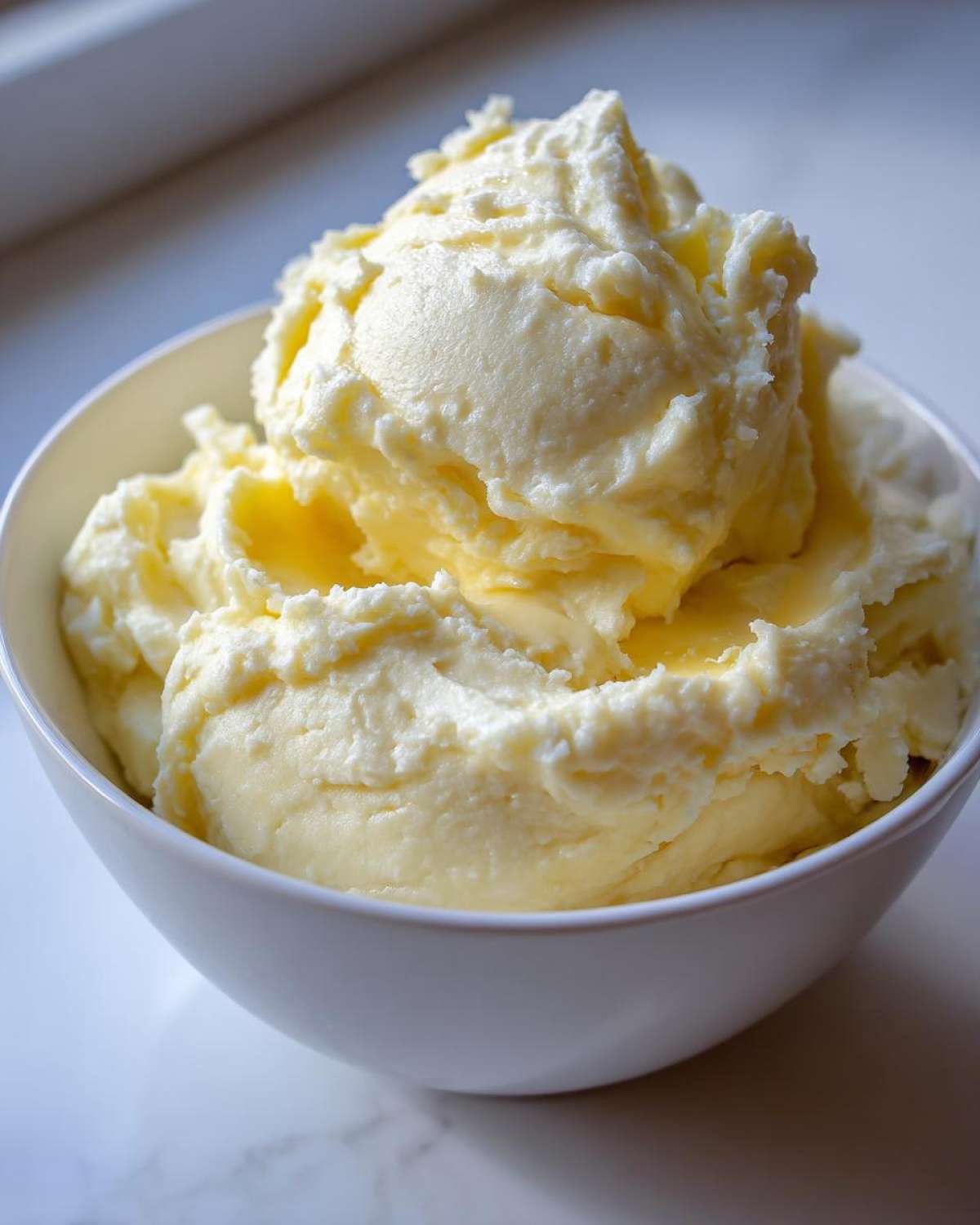 A close-up of a white bowl overflowing with rich, creamy, and fluffy mashed potatoes.