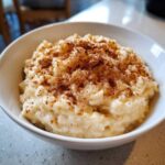 Close-up of creamy rice pudding in a white bowl, generously dusted with ground cinnamon.